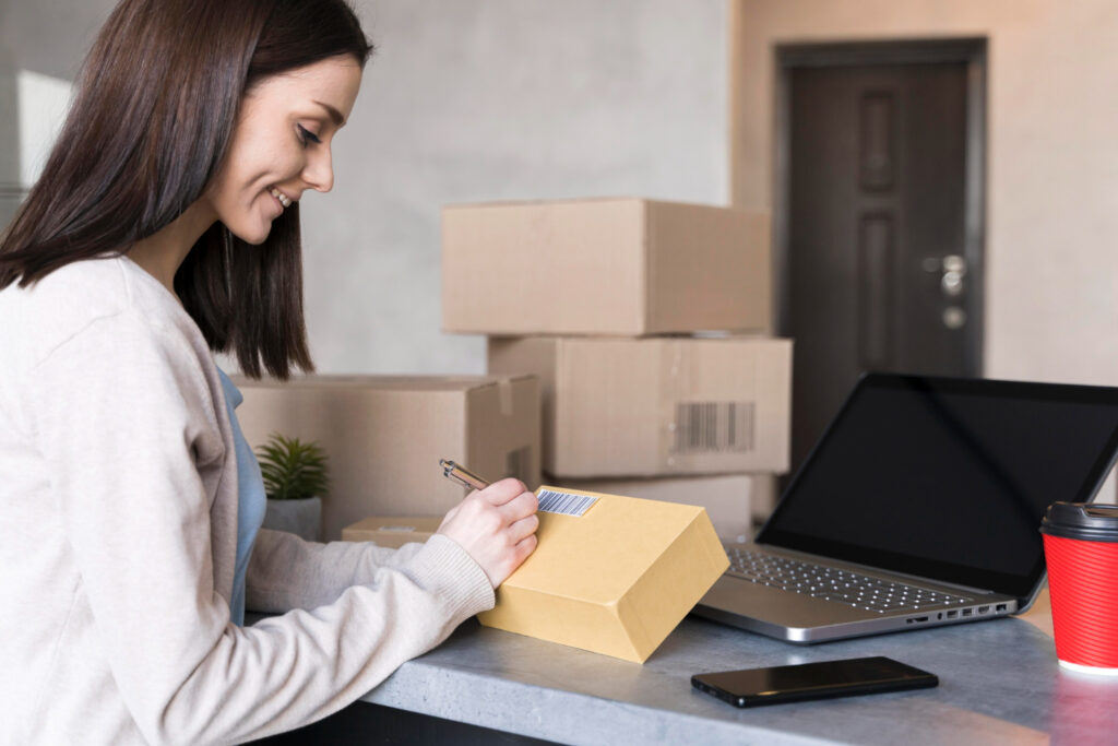 Seller 365 - A smiling woman is shown labeling a cardboard box on a desk with a laptop, smartphone, and other packages in the background.