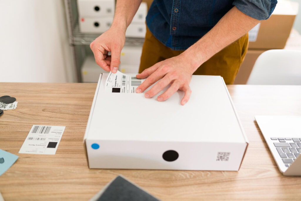Amazon FNSKU - Hands applying a barcode label to a white package for Amazon fulfillment
