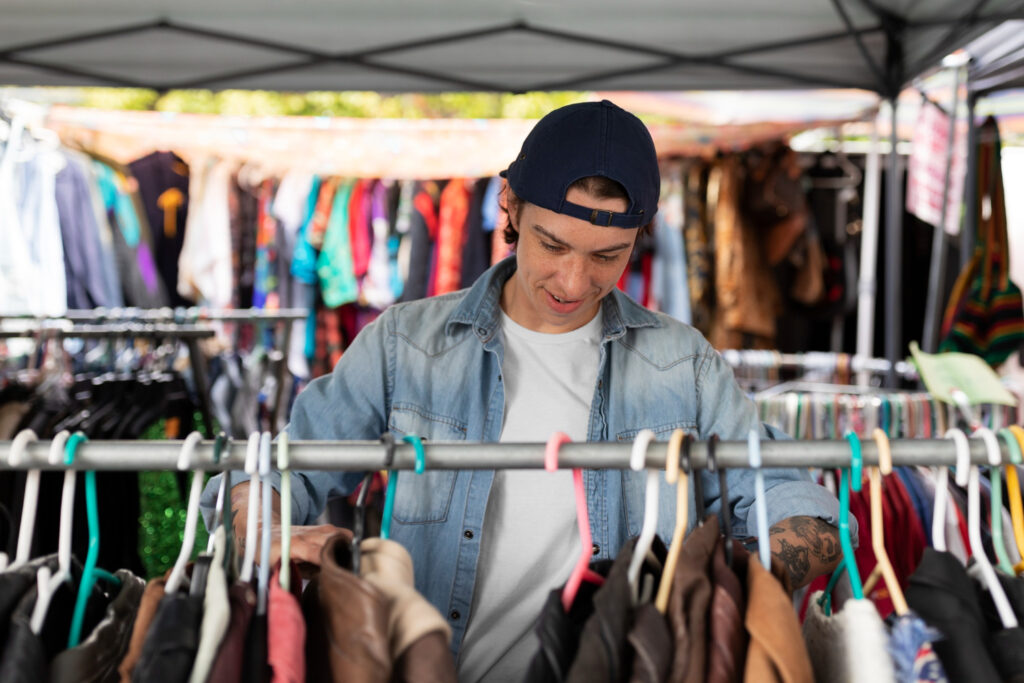 Selling used clothes online - A person browsing a rack of pre-owned clothing at a market.