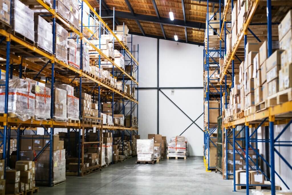 Amazon warehousing and distribution - A brightly lit warehouse aisle with high racks full of packaged inventory