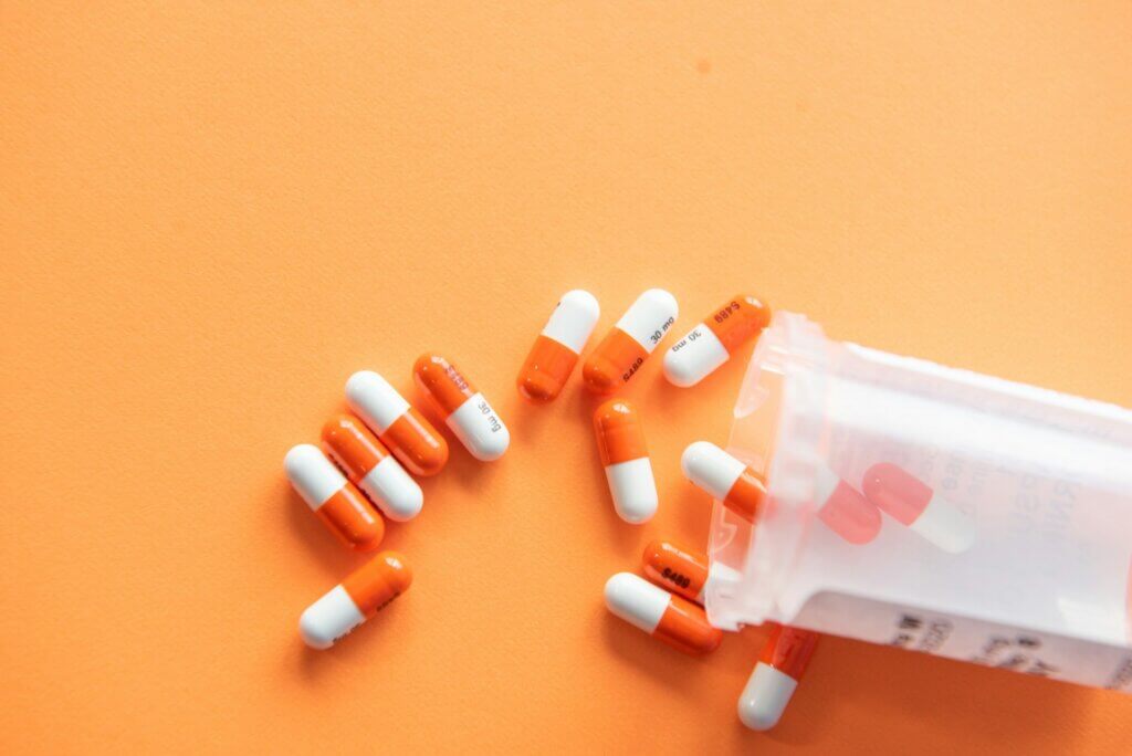 Sell supplements on Amazon - Orange and white capsules spilling out of a prescription bottle onto an orange background