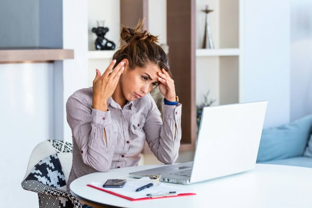 Amazon seller challenges - A woman looking overwhelmed and stressed while working on her laptop at a desk with papers