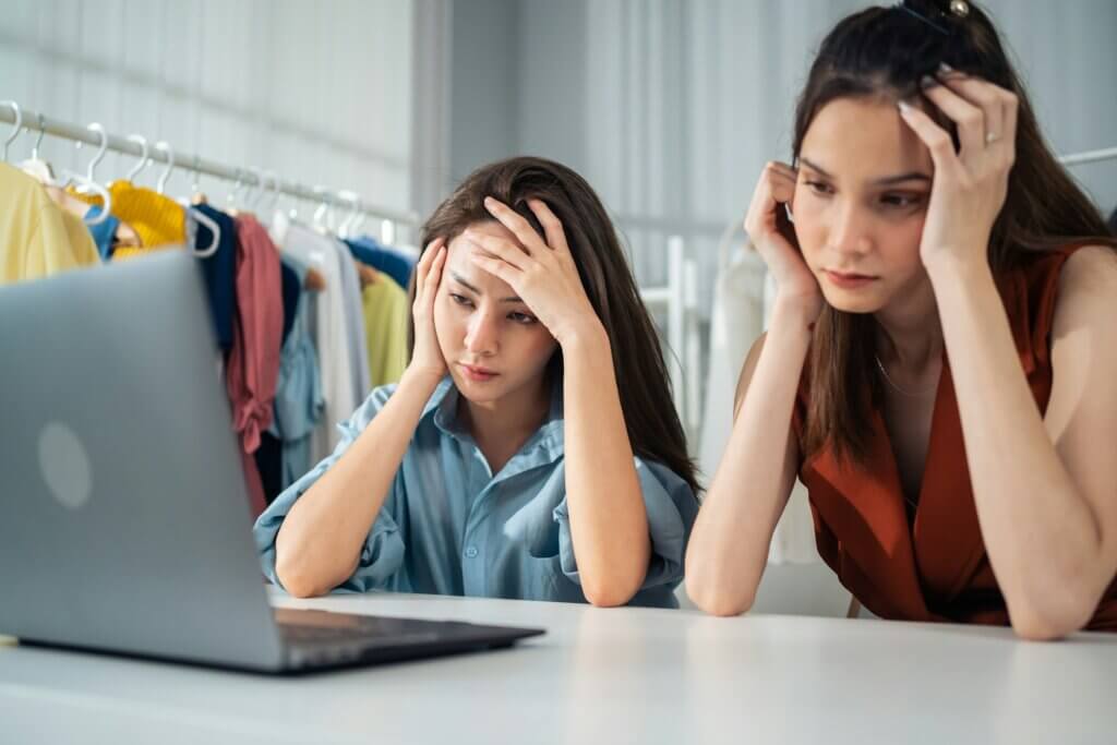 Appeal Amazon account suspension - Two women looking stressed and holding their heads while looking at a laptop in what appears to be a small business or clothing store setting