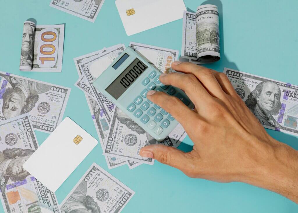 Amazon revenue calculator - A hand using a calculator on a surface covered with cash and credit cards