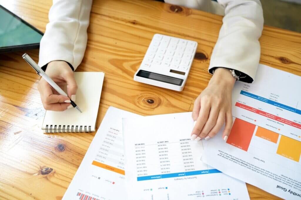 Accounting software Amazon sellers - Hands reviewing financial charts and taking notes at a wooden desk.