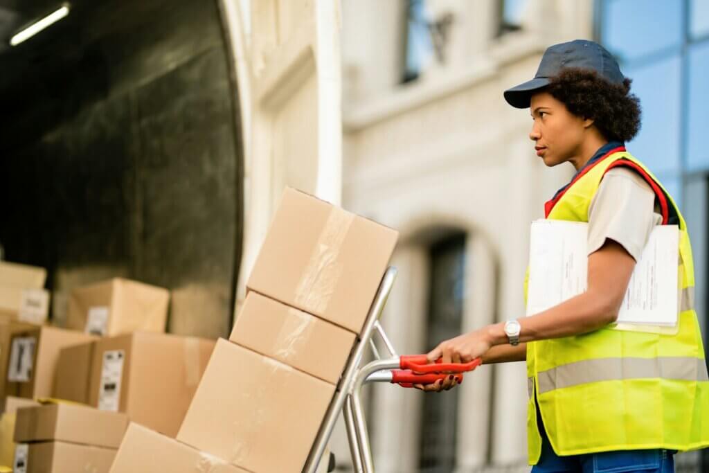 what-is-parcel-auditing - A delivery worker loading cardboard boxes onto a hand truck from a transport vehicle.